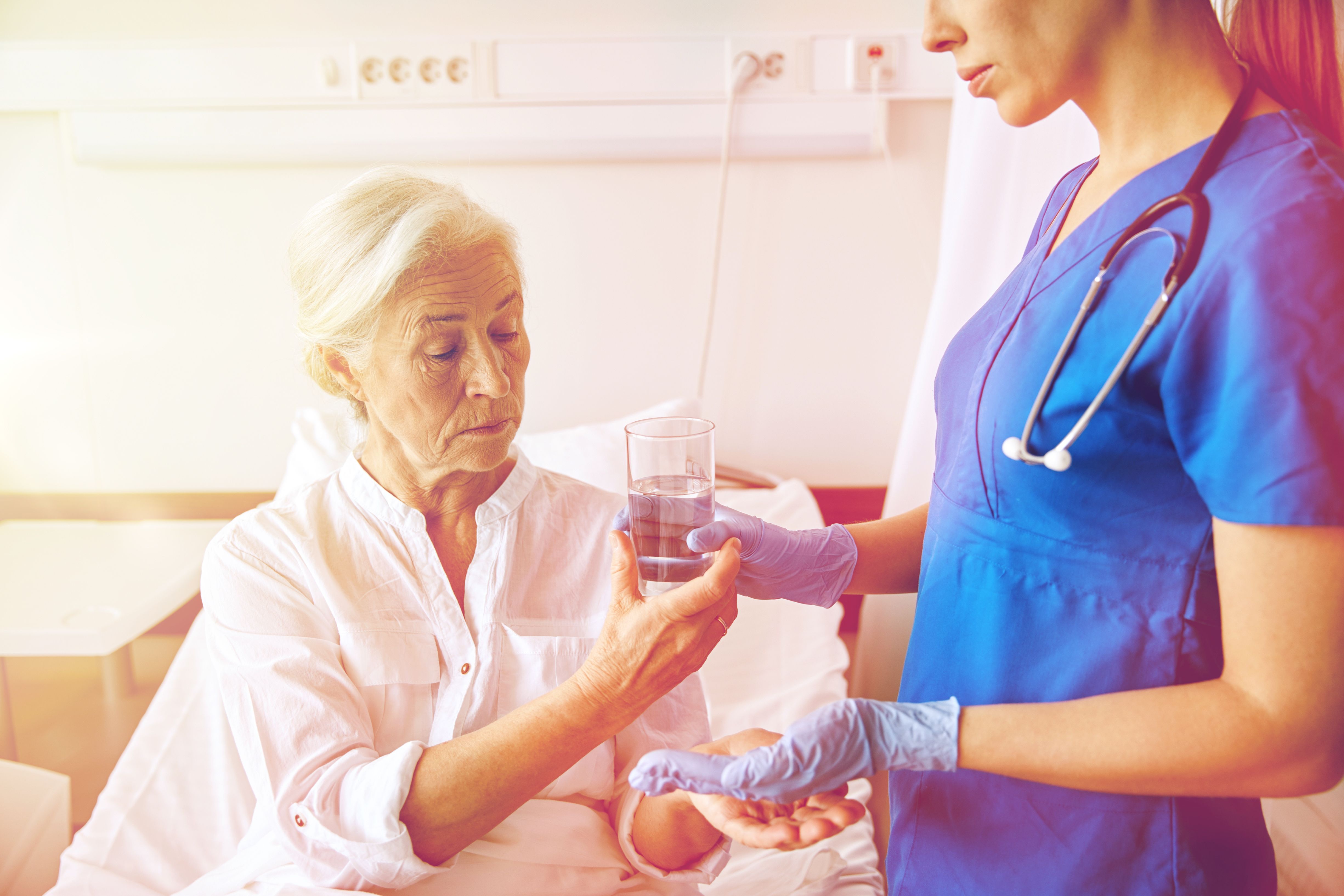 A female patient wearing a white shirt taking a pill from a nurse standing to her right