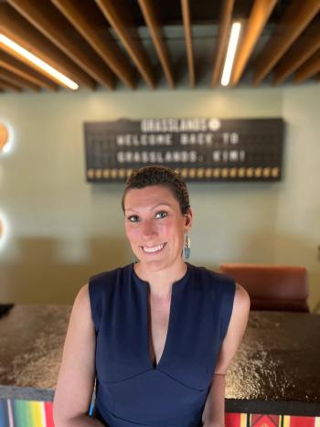 Kim Stuck, a breast cancer survivor with short brown hair, wearing a blue dress, smiles at the camera. | Photo courtesy of Allay Consulting