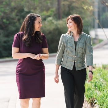Abbey Kaler wearing a purple dress, waking and talking with Alex Frenzel, who is wearing black pants and a green jacket. Photo by Diana Chavez