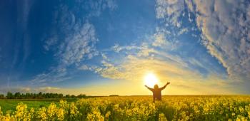 Image of a person raising their arms to the sky while standing in a field. 