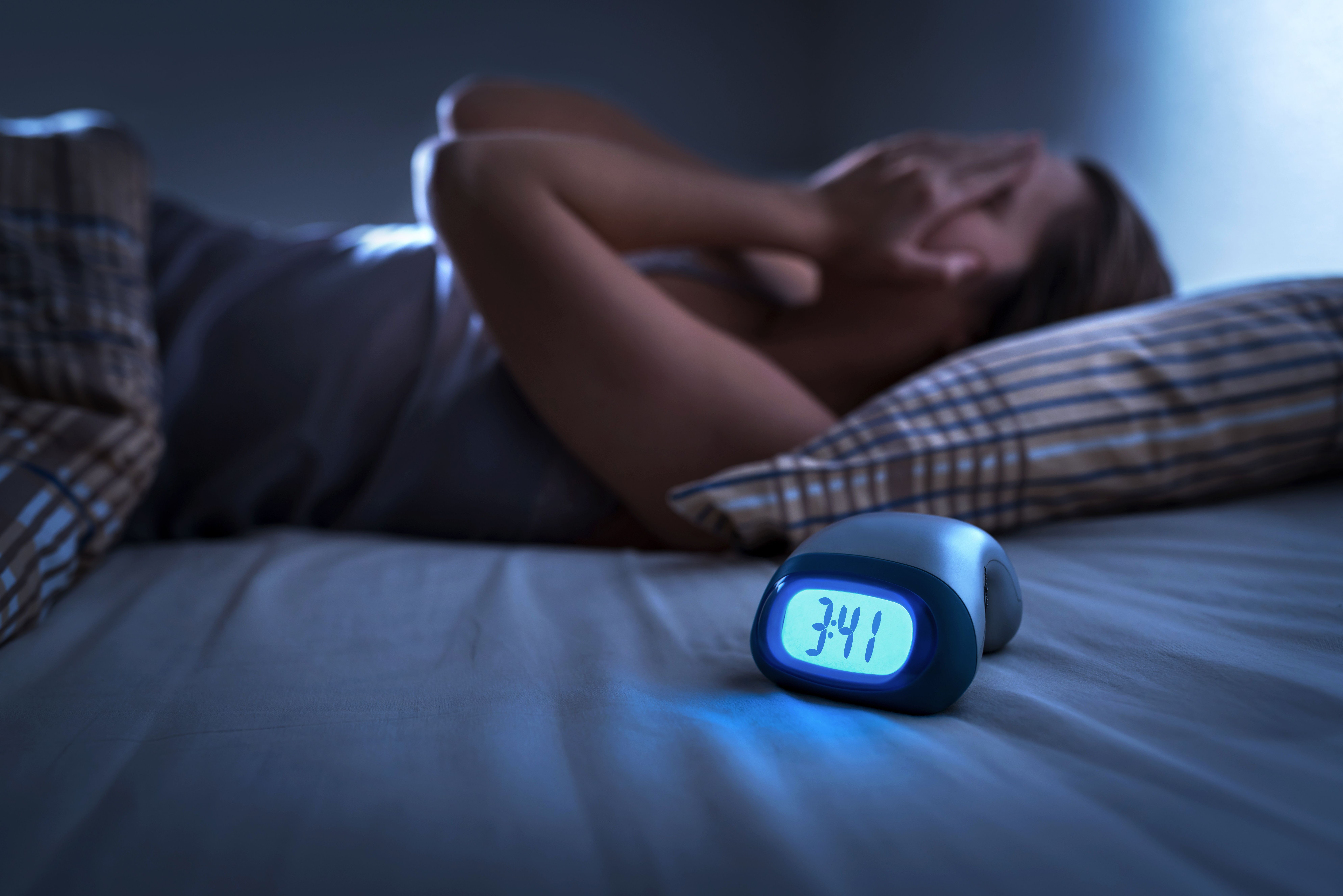 Sleepless woman suffering from insomnia, sleep apnea or stress. Tired and exhausted lady. Headache or migraine. Awake in the middle of the night. Frustrated person with problem. Alarm clock with time.  | Image credit: © terovesalainen - © stock.adobe.com