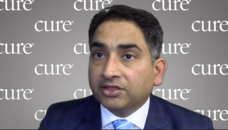 Image of a man with dark hair wearing a suit with a light blue tie.