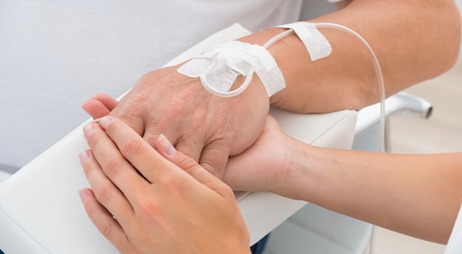 Image of a nurse holding a patient's hand while receiving chemo.