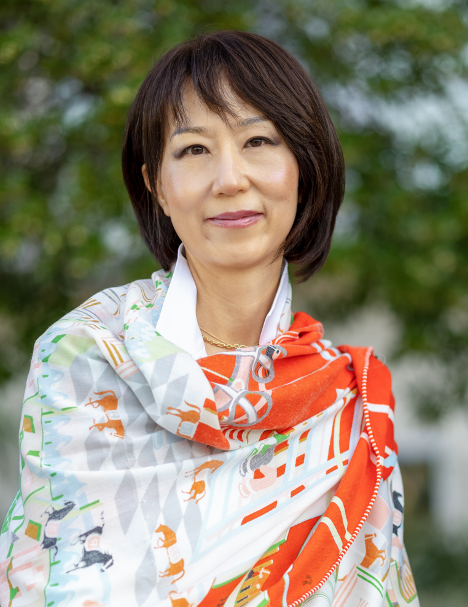 Image of a woman with a dark medium bob and bangs, wearing a white and orange shawl.