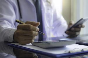 Doctor doing finances with calculator and pen
