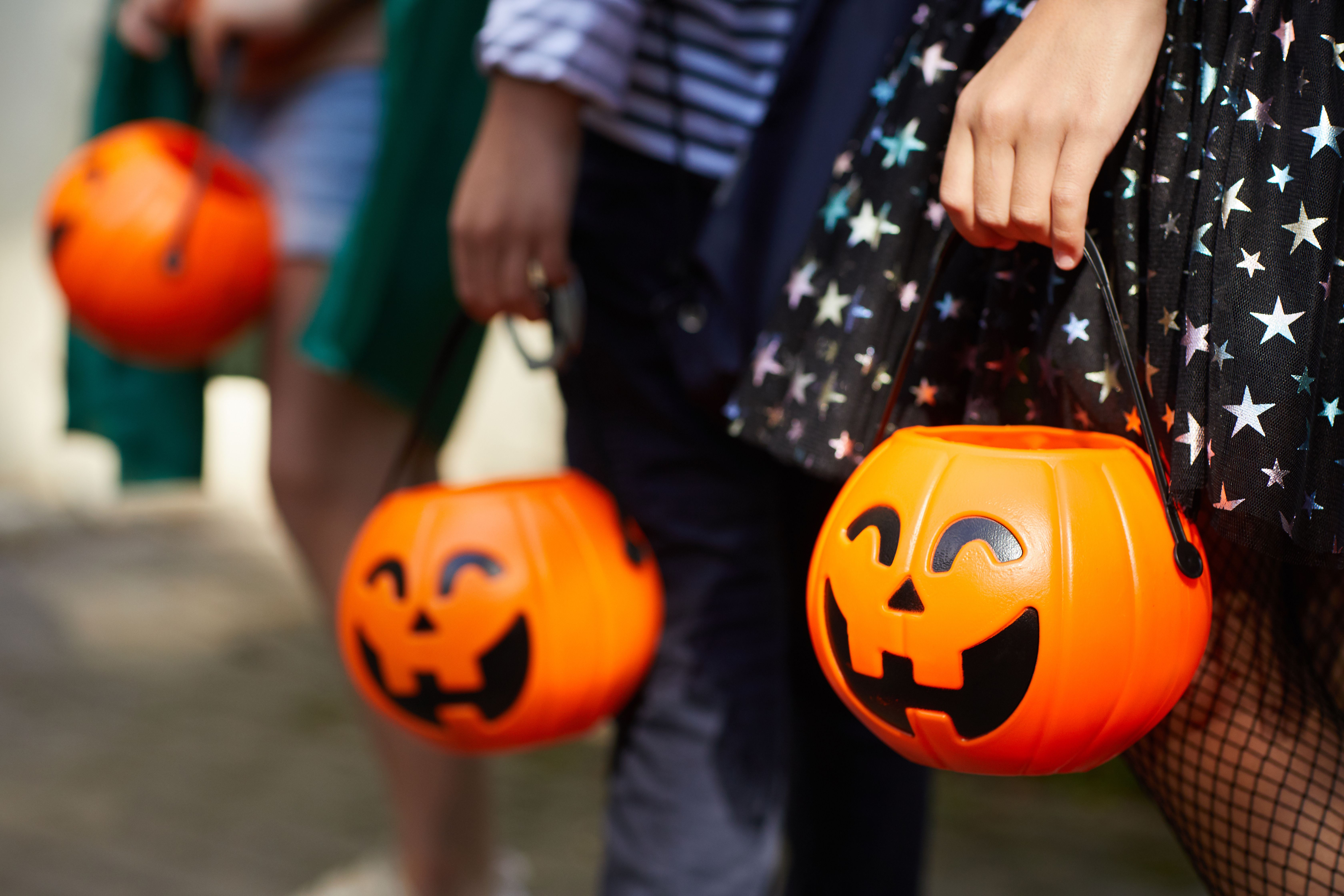 Close-up of children with pumpkins bags playing trick or treat outdoors. | Credit: Adobe Stock