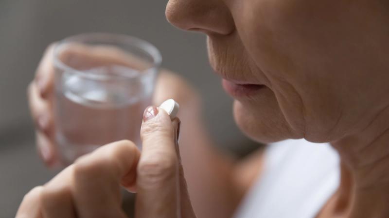 Older woman taking aspirin with a glass of water. | Credit: Adobe Stock