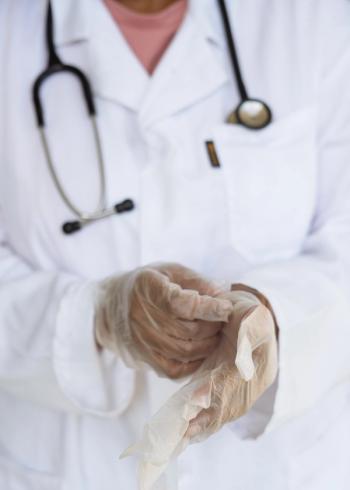 Doctor wearing a white coat putting on gloves to prepare for procedure | Credit: Pexels