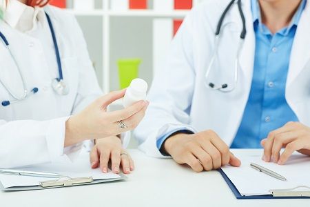 Doctors having a discussion about medications while holding a bottle containing SGLT2 inhibitors.