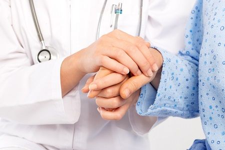 A close up photo depicting a health care provider holding the hand of a patient with cancer.
