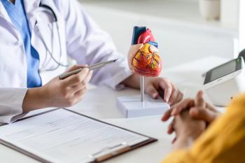 Doctor cardiologist while consultation showing anatomical model of human heart with aged patient talking about heart diseases.