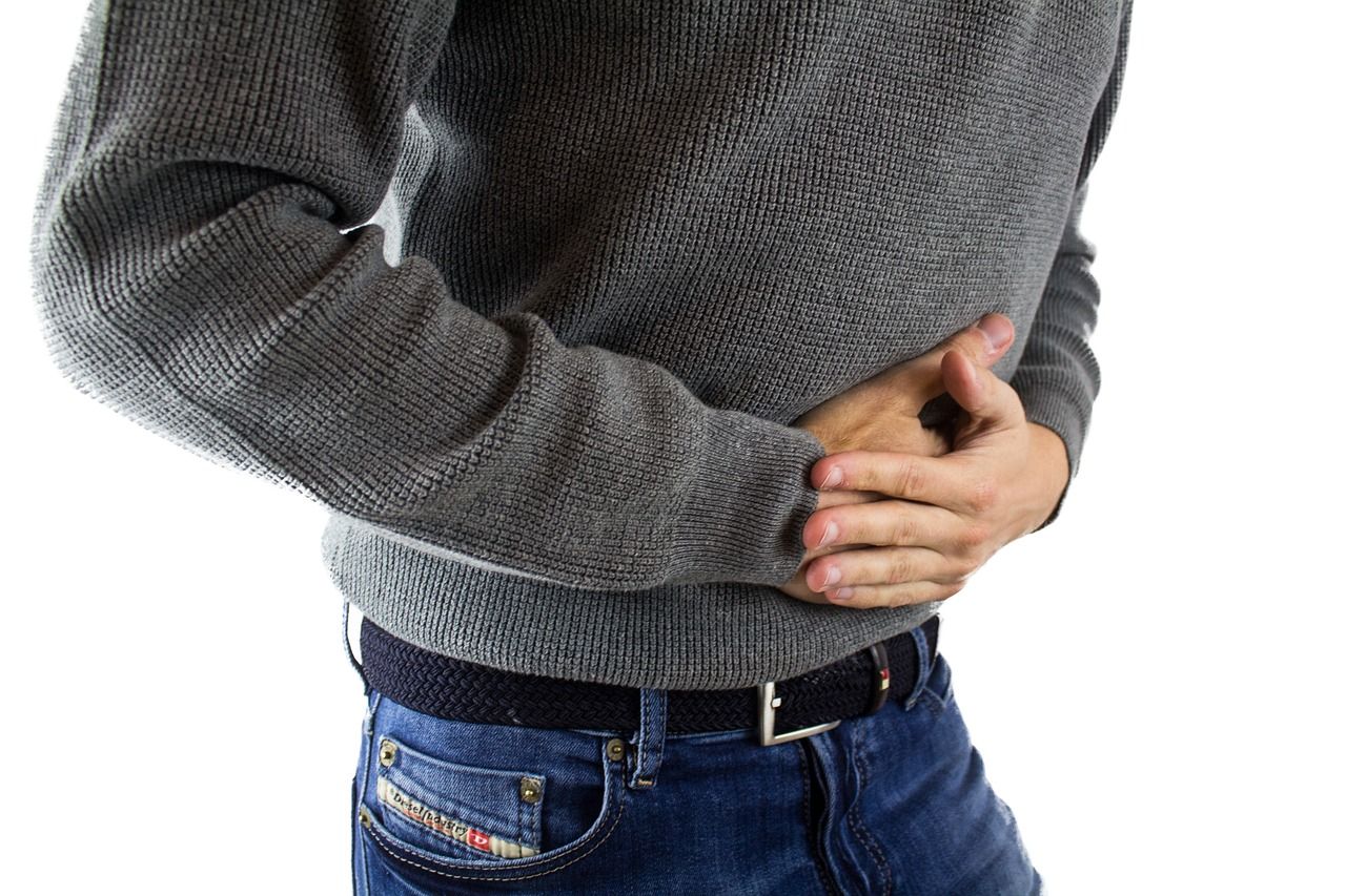 Person wearing gray sweater holding abdomen in pain | Credit: PixaBay