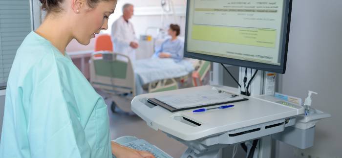 Nurse typing on portable computer keyboard workstation in hallway outside patient room
