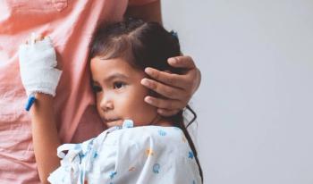 Child in hospital gown holding onto nurse in pink scrubs