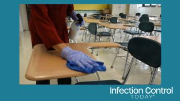 Teacher with a spray bottle, gloves, and a rag, wiping, cleaning, and disinfecting school desks.  (Adobe Stock 632161219 by Robert Peak)
