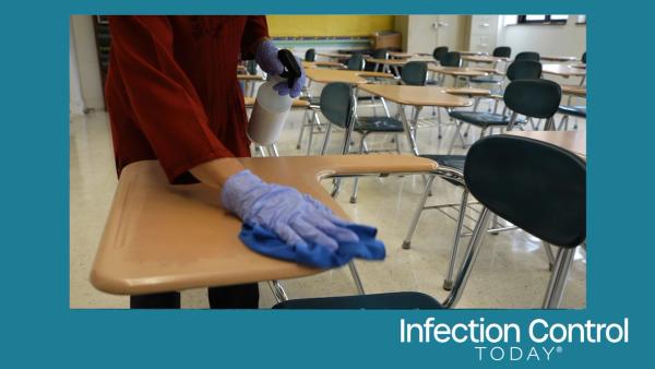 Teacher with a spray bottle, gloves, and a rag, wiping, cleaning, and disinfecting school desks.  (Adobe Stock 632161219 by Robert Peak)