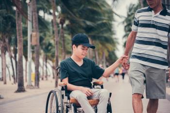 Boy wearing back cap in wheelchair holding hand of male adult | image credit:©Gayson stock.adobe.com