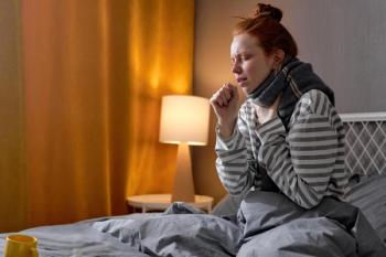 A woman with red hair in bed with a scarf around her neck coughing | image credit: ©alfa27