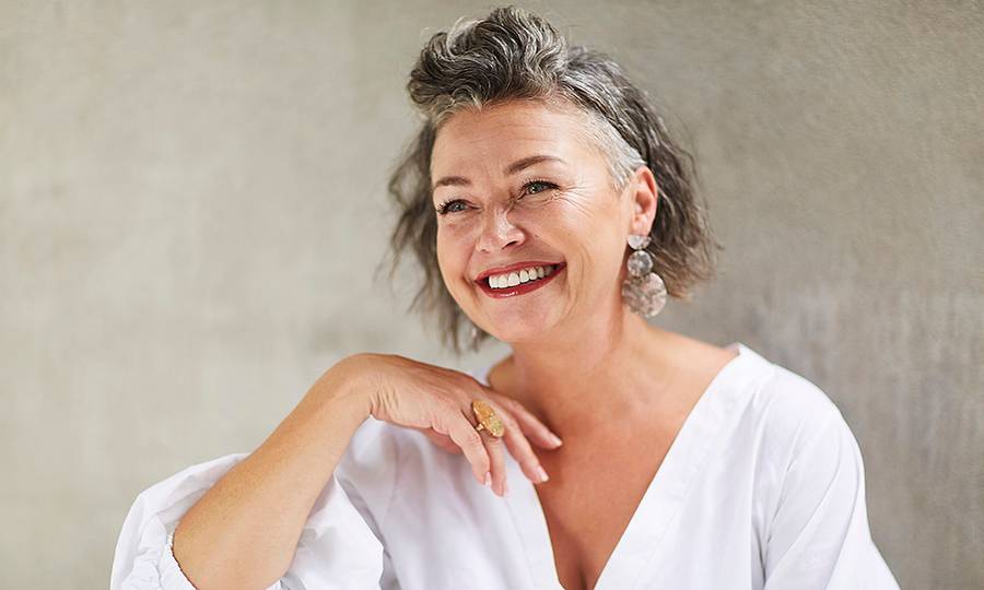 Happy mature woman sitting in front of gray wall