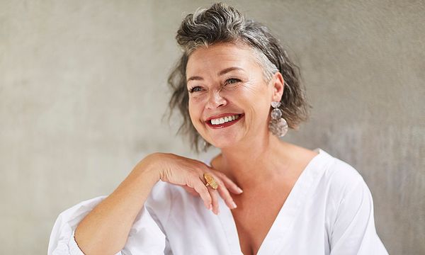 Happy mature woman sitting in front of gray wall