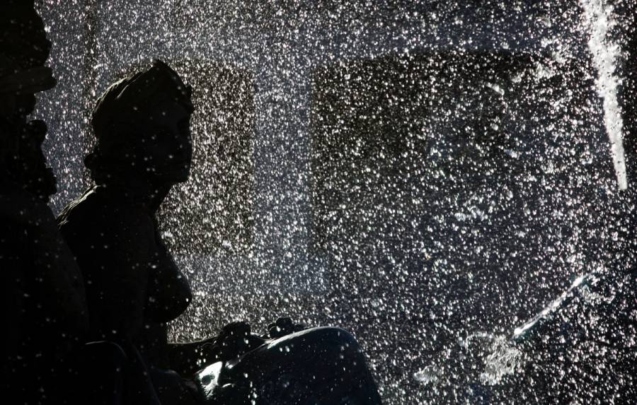 A classical statue silhouetted against glittering, backlit fountain spray