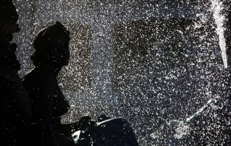 A classical statue silhouetted against glittering, backlit fountain spray