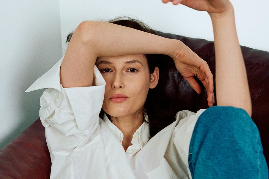 Mature woman in white shirt sitting on couch with arms up over head