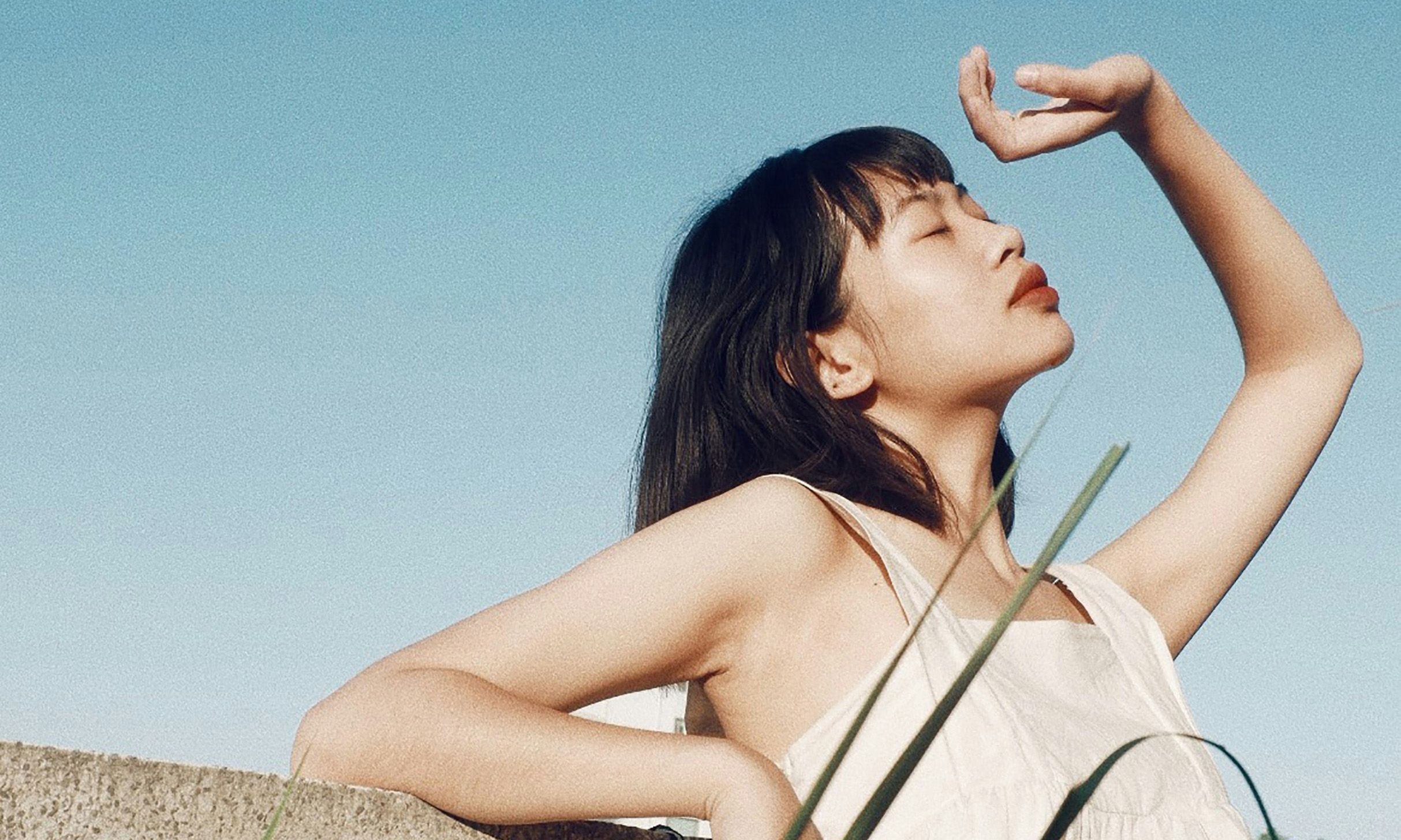Asian woman outdoors looking up to sky with eyes closed and hand over her face