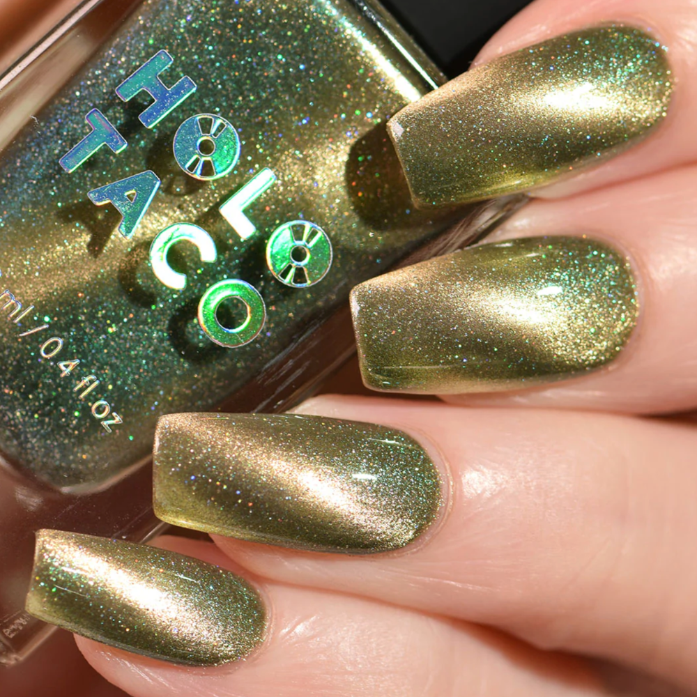 A closeup of a woman's fingers with green colored nails touching a bottle of Holo Taco Menchie Cat Eye nail polish