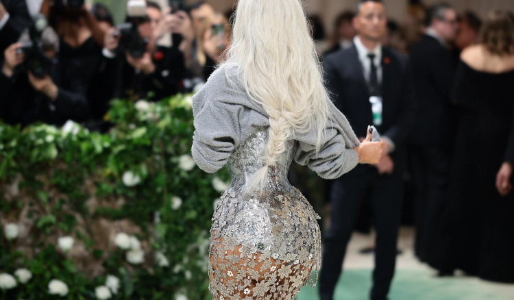 Kim Kardashian, seen from behind, in a silver floral-embellished corset gown with a gray sweater over her shoulders and a long platinum braid.