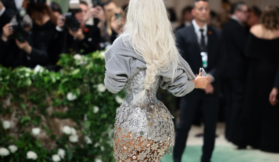Kim Kardashian, seen from behind, in a silver floral-embellished corset gown with a gray sweater over her shoulders and a long platinum braid.