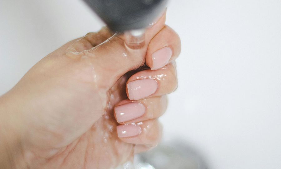 hand with pale pink manicure rinsing under a faucet