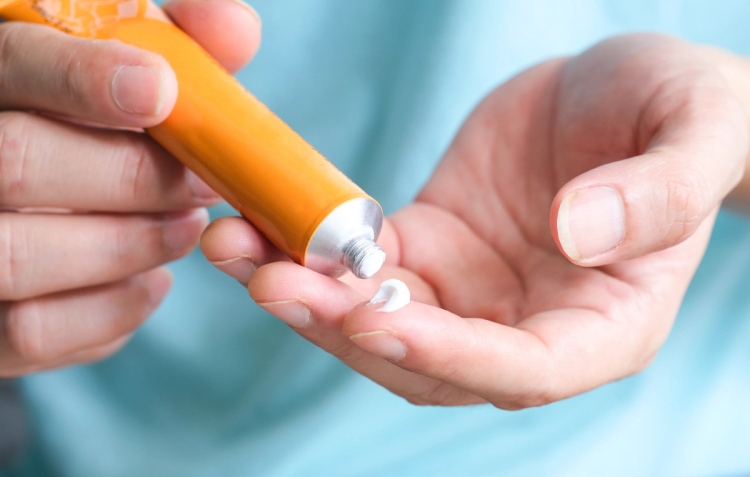 Close-up of a hand squeezing white cream from an orange tube onto fingers