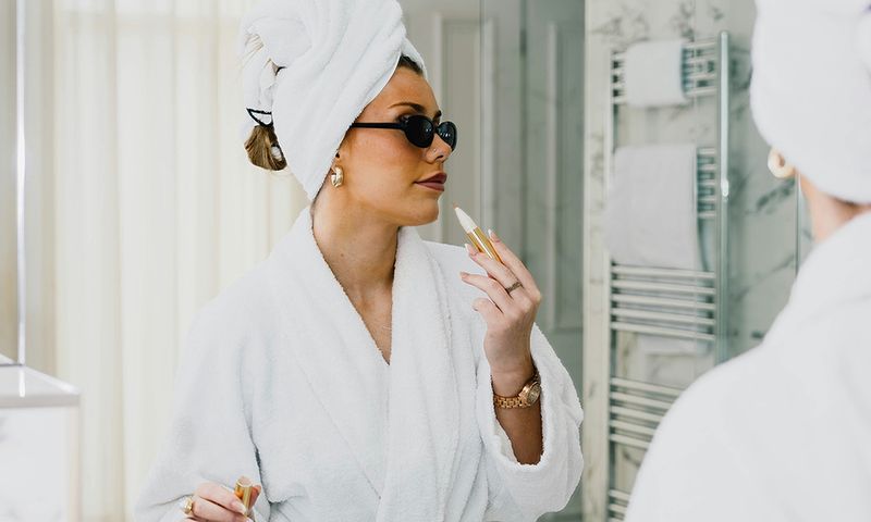 woman in sunglasses and bathrobe putting on makeup