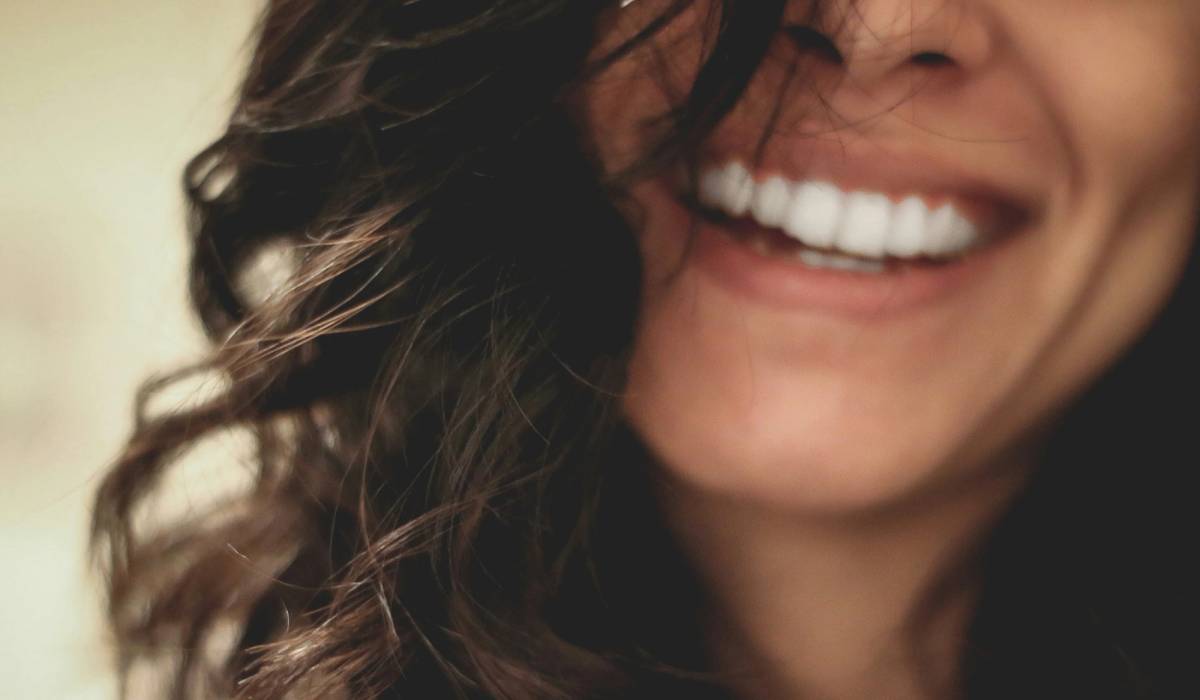 Close-up of a woman with wavy brown hair laughing, showing a bright white smile