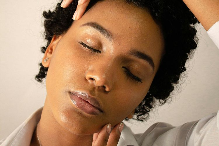 black woman with eyes closed touching face and head