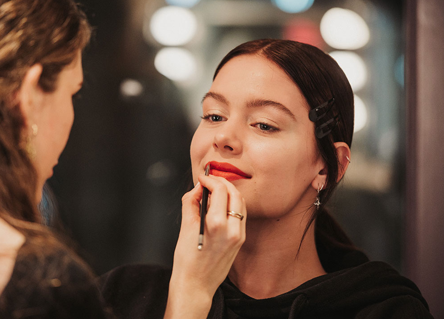 Brunette woman getting her red lipstick applied by a makeup artist