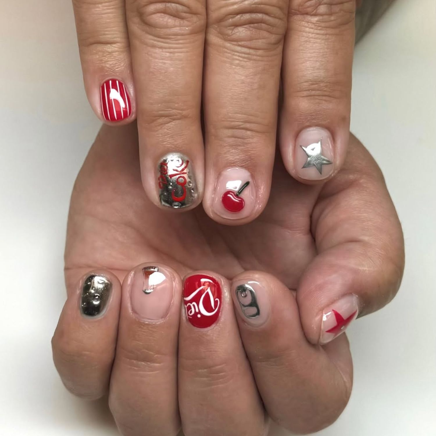 Short soda-inspired nail art featuring sheer natural nails with red logo details, silver chrome accents and pop-top designs