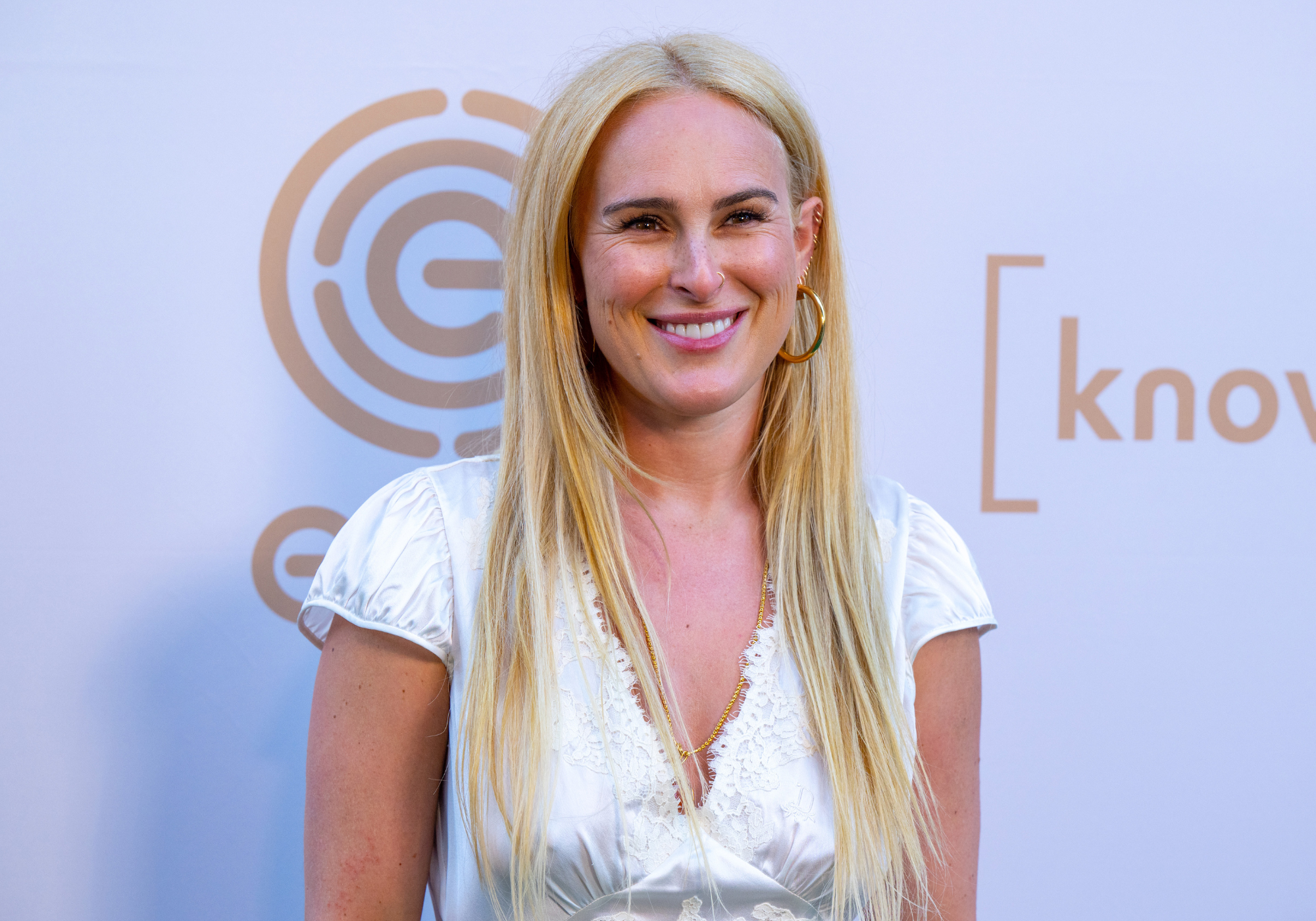 Rumer Willis smiles at a red carpet event wearing a white top and long blonde hair
