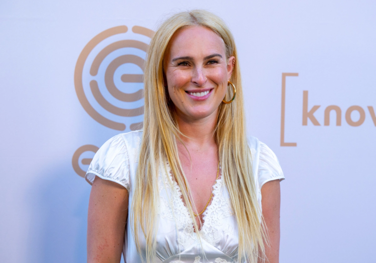 Rumer Willis smiles at a red carpet event wearing a white top and long blonde hair