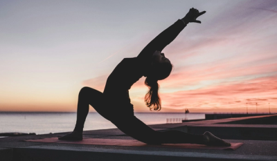 Woman in a backbend yoga pose on a pier at sunset, arm raised toward the sky.