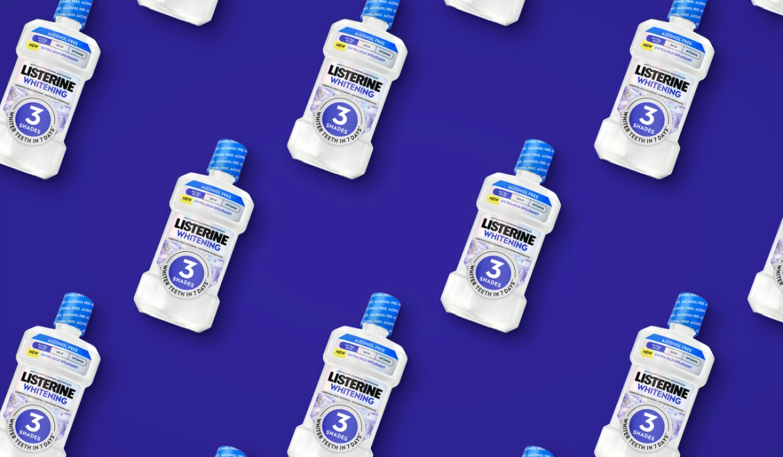 Repeating pattern of Listerine Whitening Extra Mild Spearmint mouthwash bottles, tilted diagonally on a deep indigo background.