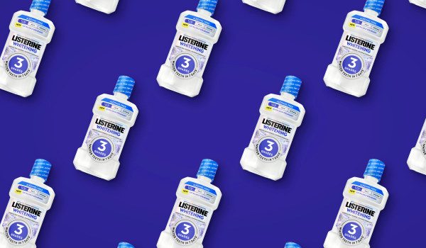 Repeating pattern of Listerine Whitening Extra Mild Spearmint mouthwash bottles, tilted diagonally on a deep indigo background.