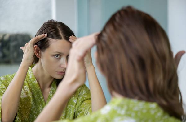woman looking at hairline in mirror