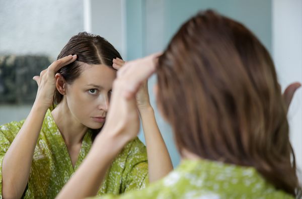 woman looking at hairline in mirror