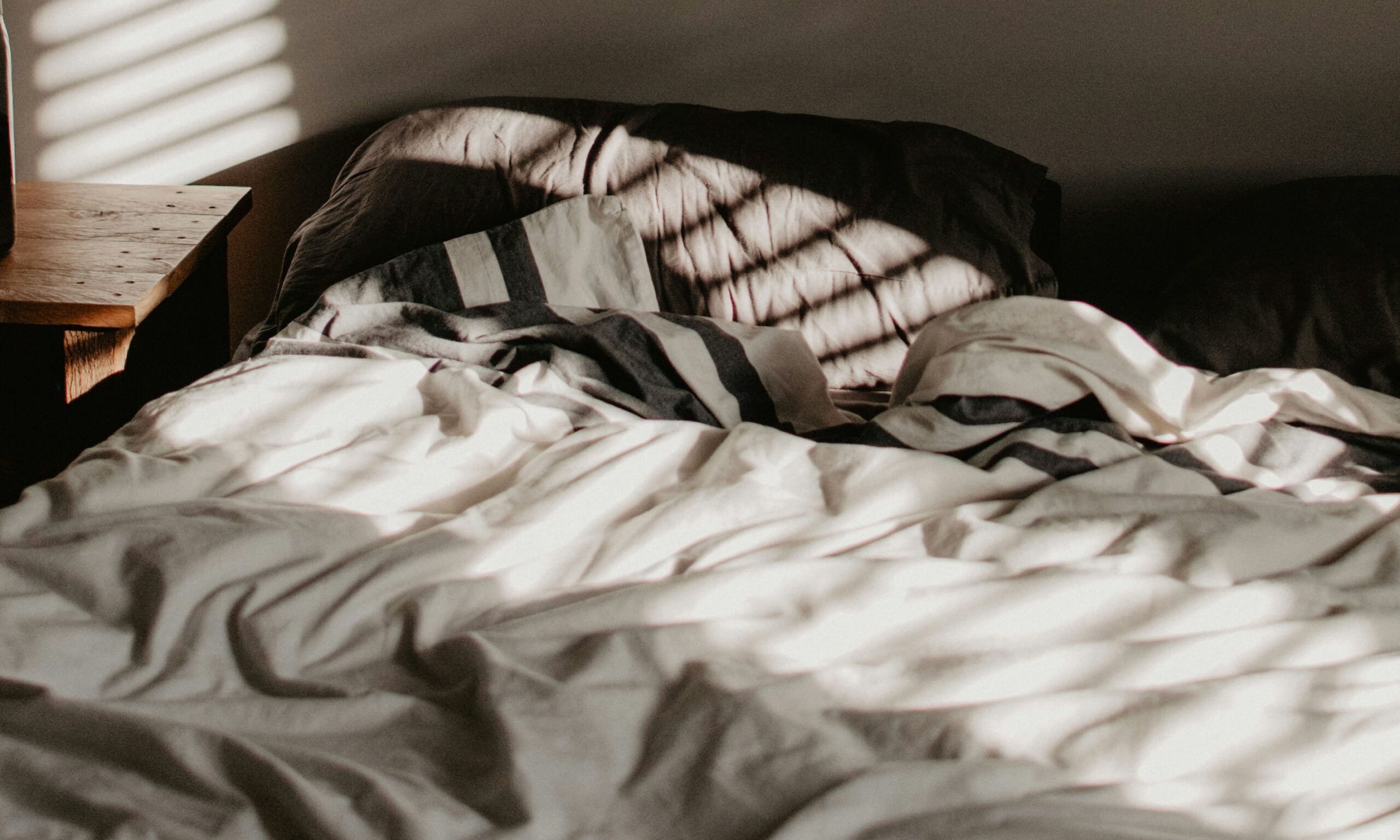 Empty bed in sunlit shadowed room with ruffled sheets