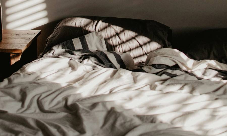 Empty bed in sunlit shadowed room with ruffled sheets