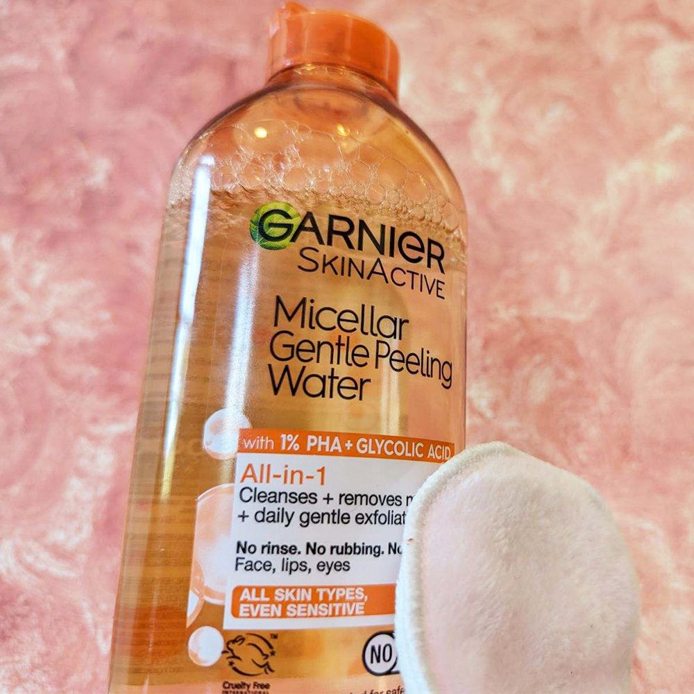Garnier's Micellar Gentle Peeling Water and reusable eco pad in front of a pink background. A micellar water for makeup removal.