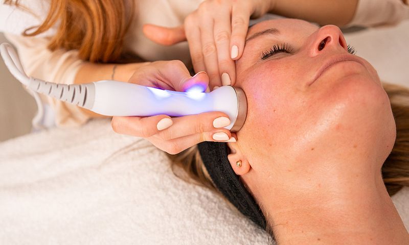 Vertical photo of a woman at the spa getting a rejuvenation treatment on her face using ultrasound and light therapy