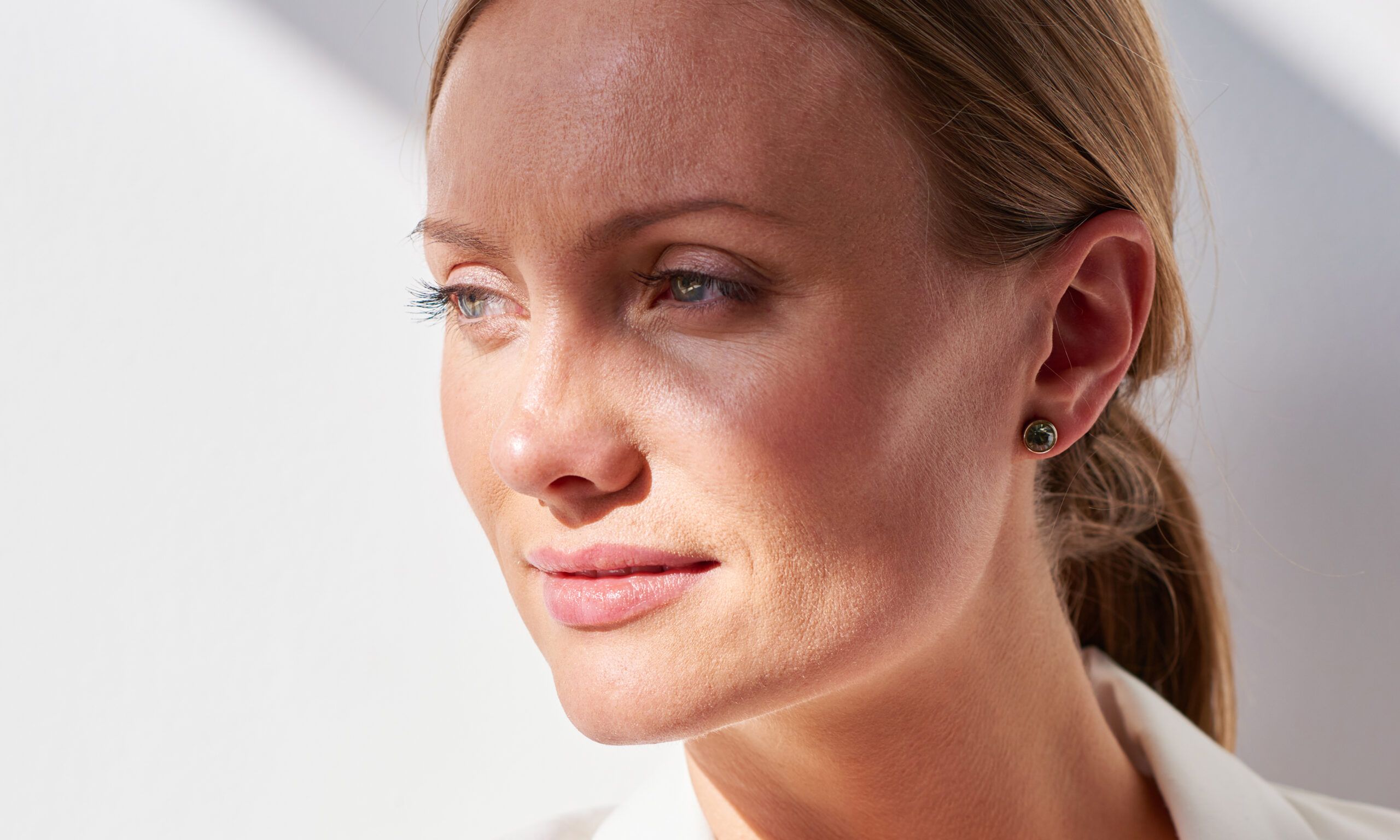 Adult modern woman in stylish white jacket looking pensively away on white background in bright sunlight